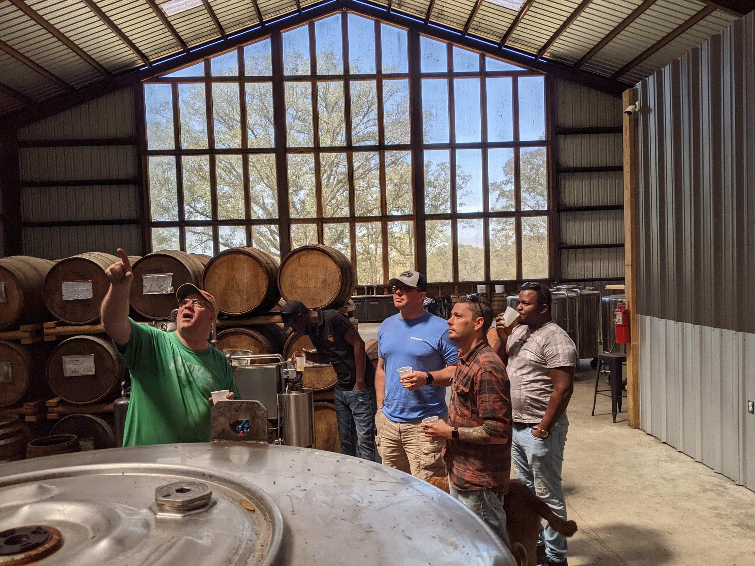 Cam pointing up at the still during a distillery tour. a large white oak is visible through a floor to ceiling window wall.