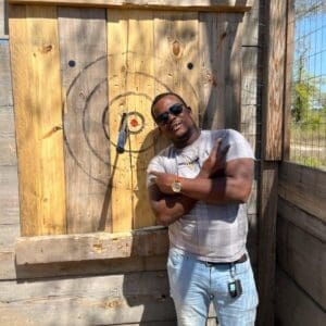 Gentleman standing next to axe stuck at the Timber Creek Distillery axe throwing range.