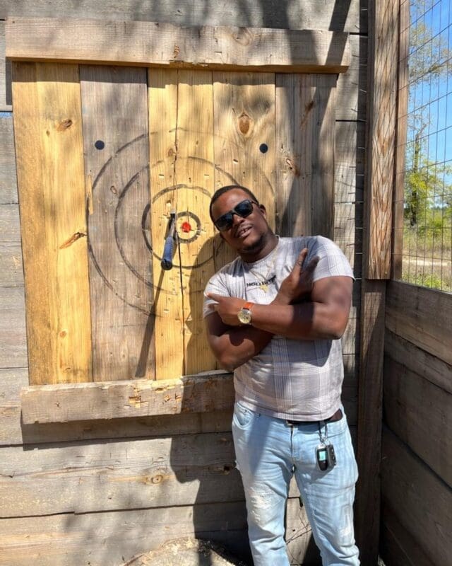 Gentleman standing next to axe stuck at the Timber Creek Distillery axe throwing range.