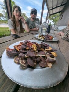 A plate of chocolate covered fruit with a couple customers drinking wine in the back.